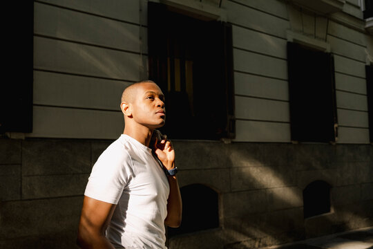 Black man holding sunglasses in dramatic urban street style portrait