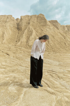 Woman stands in sand area with tall rock formations in background