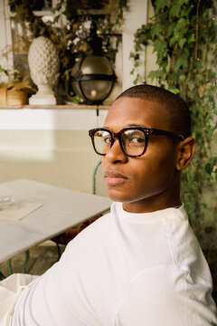 Man in glasses posing in white shirt at leafy outdoor cafe