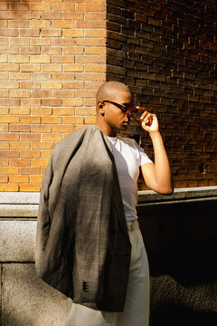 Man adjusting sunglasses brick wall street editorial fashion portrait