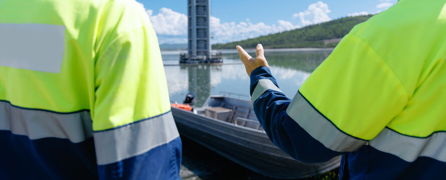 Two workers pointing at aluminum boat near reservoir dock, gold mining tailings impoundment.