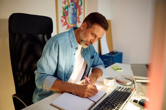 Man Writes in a Notebook at a Desk