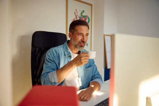 Man sits at a desk in the home office, drinking coffee