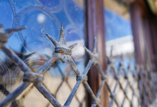 Ornate wrought iron window grille with pointed spikes and decorative patterns, reflecting sunlight and showcasing a glimpse of the Venetian architecture behind