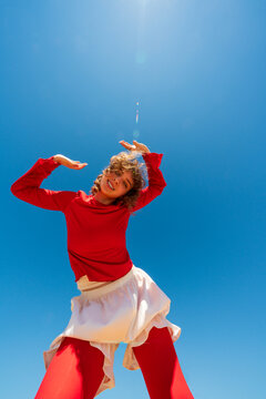 Smiling woman posing with raised hands under blue sky