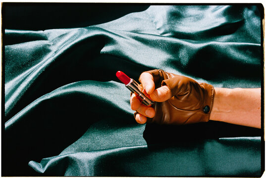 a man holds a red lipstick above rippling dark green fabric, 35mm film