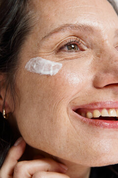 A Woman is Smiling as She Applies Cream to Her Cheek