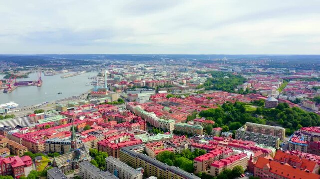 Gothenburg, Sweden. Aerial panorama over the historic city center with red-tiled rooftops, the winding Gota Alv river, and distant harbor cranes under an overcast summer sky.. Drone footage
