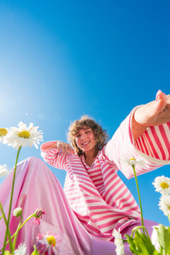Smiling woman in pink outfit reaching through daisies