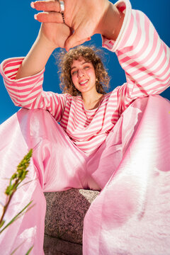 Smiling woman in pink outfit framing camera with hands