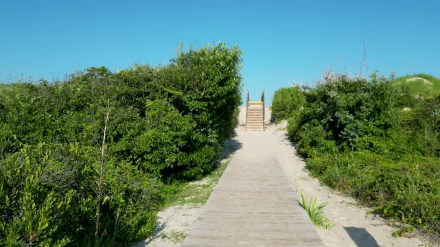 Drone rising over a wooden boardwalk and the sand dunes to see the Atlantic Ocean and Beach in Corolla North Carolina.