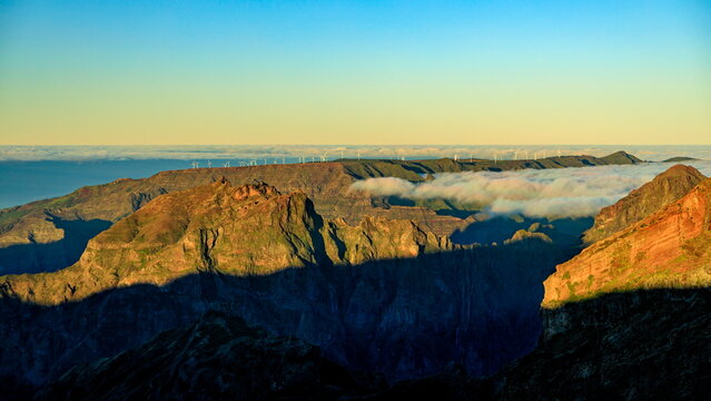 Juncal, Portugal - 05.12.2025: Golden light hits rugged peaks above a thick cloud inversion with wind turbines on the distant ridge