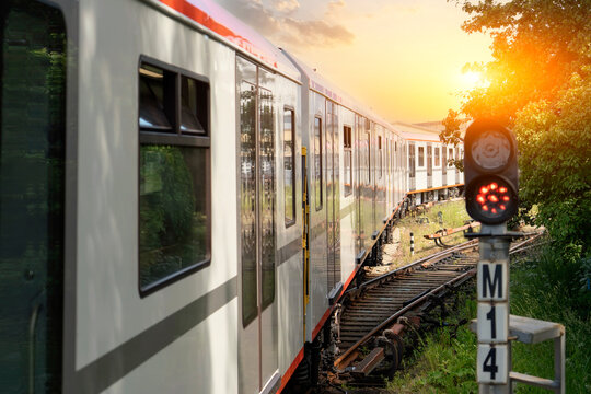 A train gently curves along the tracks, with warm sunlight casting a golden hue on its sleek exterior. Trees frame the scene, enhancing the tranquil atmosphere.