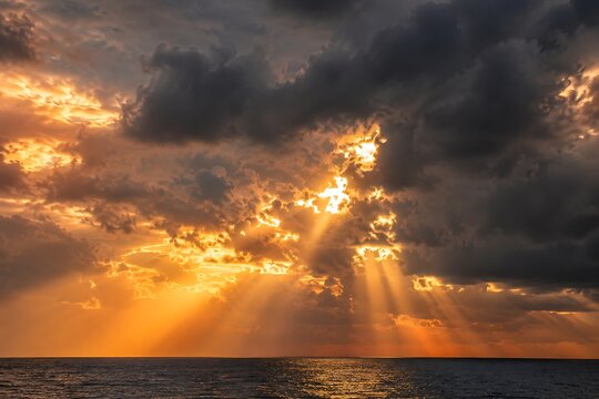 Golden sun rays breaking through dramatic storm clouds above the dark ocean horizon