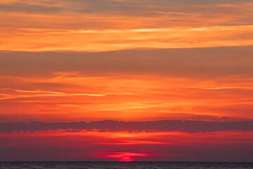 Fototapeta premium Vibrant orange sunset over calm ocean horizon with layered atmospheric clouds at dusk