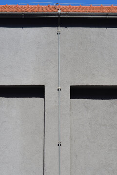 Vertical lightning conductor wire secured with metal clamps on a textured gray plaster facade of a modern residential building.