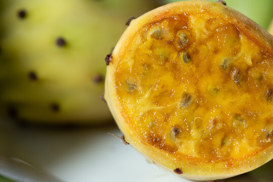 Fresh prickly pears are arranged on a plate. One prickly pear has been cut open.