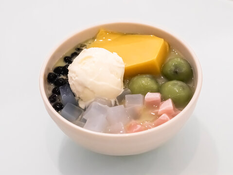 A bowl of Asian shaved ice dessert topped with a scoop of vanilla ice cream, yellow pudding, green mochi balls, tapioca pearls, and colorful jelly cubes.