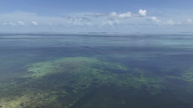 Aerial drone footage over the clear turquoise shallows and seagrass flats of the Florida Keys with distant islands on the horizon