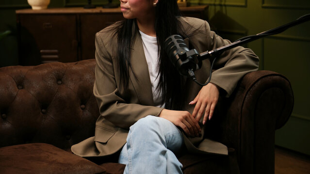 Woman sitting on a leather couch, recording a podcast with a studio microphone