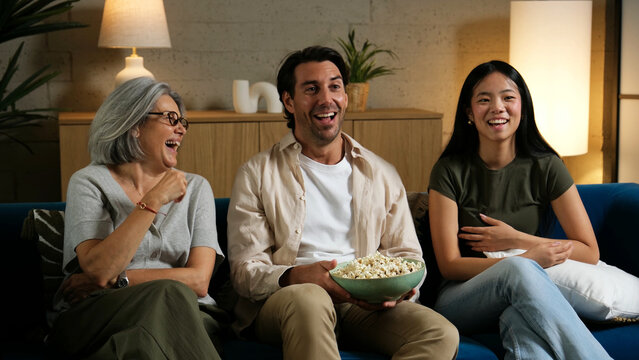Multi ethnic family laughing while enjoying popcorn and cinema at home