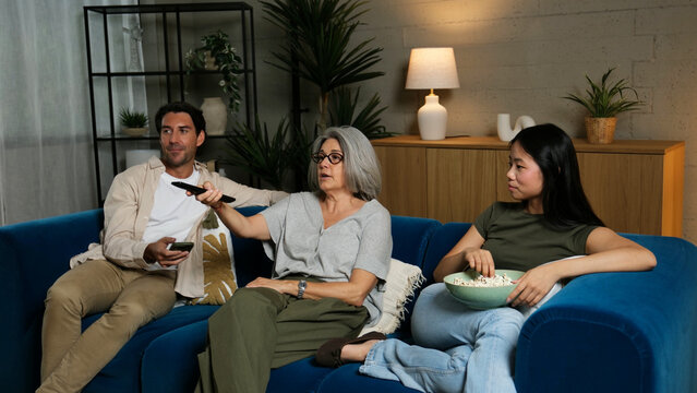 Family members sitting on sofa, watching TV and eating popcorn at home