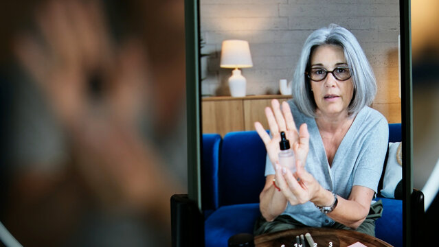 Mature woman presenting skincare product on video call, sharing beauty tips
