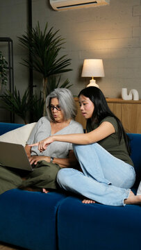Mature woman and young female adult sitting on a couch, learning and connecting with technology