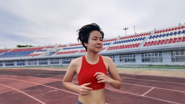 Side view of Asian woman jogging on a stadium track. This outdoor fitness concept highlights a healthy lifestyle, cardiovascular exercise, endurance training, and an energetic daily running routine.
