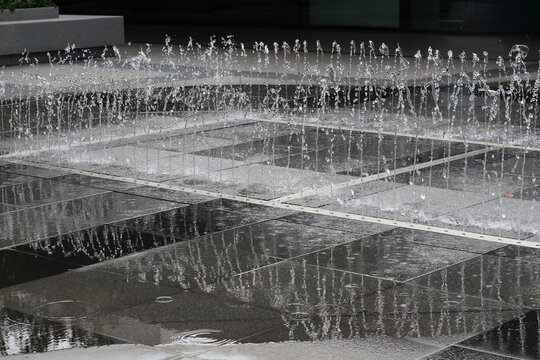Modern water feature with rhythmic jets spraying water onto polished stone tiles