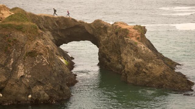 A couple walks and plays near the arch at Mendocino Headlands State Park while enjoying views of the foggy ocean and coastline.