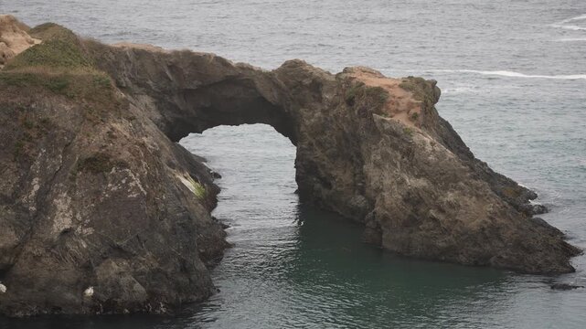 View the arch at Mendocino Headlands State Park as it stands over the ocean along the Pacific coastline in California under fog.
