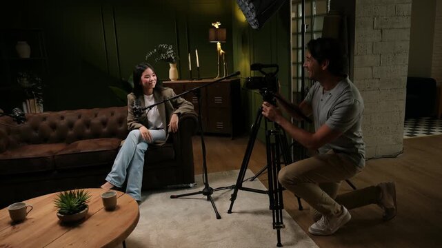 Professional cameraman filming a young Asian woman giving an interview for a podcast in a studio