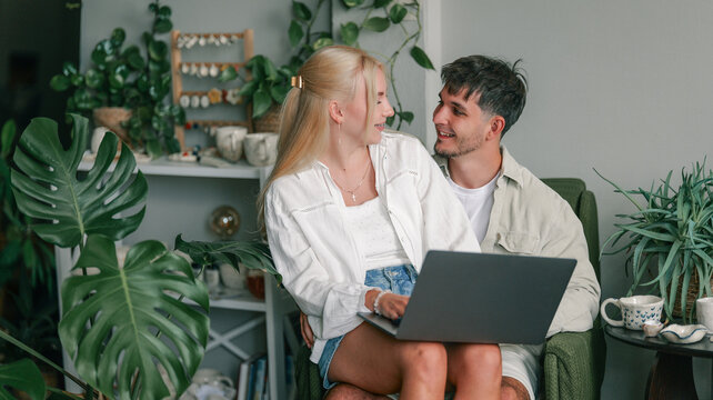 Young couple happily interacting while using a laptop together at home