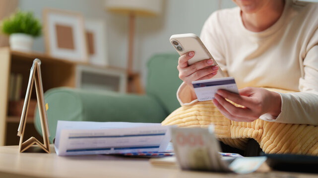 Woman using smartphone while holding payment card at home, online payment, mobile banking, digital transactions, e-commerce and cashless consumer finance