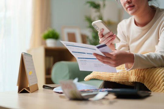 Woman checking household bills with smartphone and payment card at home, concept for online bill payment, monthly expenses, budgeting, mobile banking and financial planning