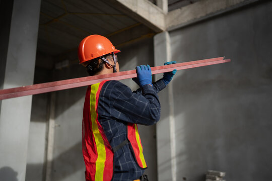 Construction Worker Carrying Steel Beams at an Unfinished Building Site