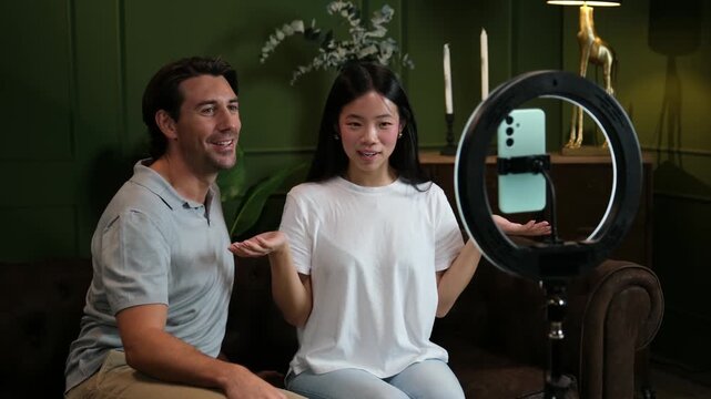 Multiracial couple of bloggers streaming online with a smartphone and a ring light at home
