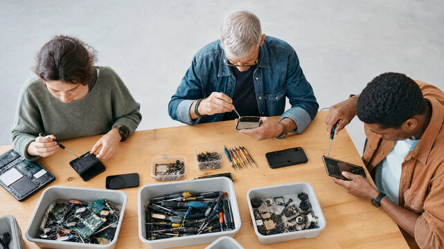 Electronic repair technicians working on smartphones, diverse team fixing mobile devices at wooden table, tech support workshop
