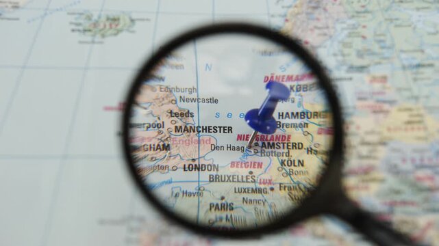 Magnifying glass reveals marked location on printed paper map showing Manchester