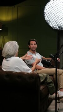 Senior woman and a young man talking and gesturing during a live podcast in a professional studio