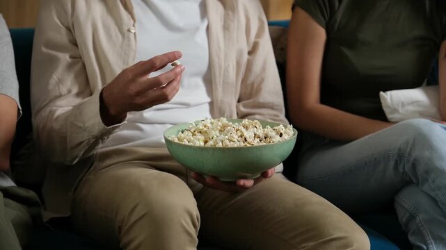 Close up of a multigenerational family sharing a bowl of popcorn while sitting on a couch