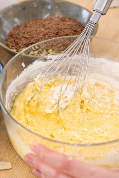 Pastry preparation. Homemade recipe. Female baker hand stirring whisk yellow dough at kitchen table with flax seeds bowl for healthy food.