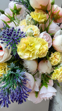 Colorful artificial flower arrangement with yellow, pink and blue blossoms, green leaves and decorative foliage, close-up floral composition for interior decor.