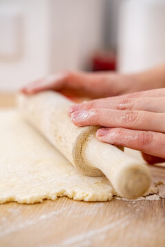 Culinary process. Rolling dough pin. Female baker hand preparing sweet pastry treat on home wooden kitchen table covered with flour.