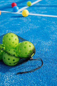 Close up of bright green neon pickleball balls packed in a black mesh net bag resting on a blue court