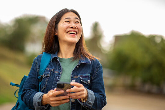 Happy East Asian woman using smart phone outdoors in nature