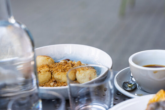 Sweet cottage cheese dumplings with breadcrumbs and nuts served in a bowl with coffee on a cafe table