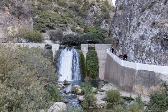 Small waterfall flows through rocky gorge surrounded by vegetation and bounding walls, El Kelaa in Morocco