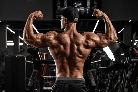 Muscular man showing back musclesin gym. Strong male rear view